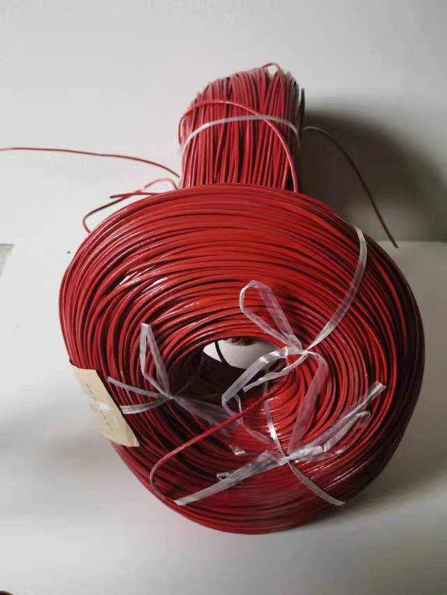 A large flat coil of red TS thermosensitive cable cross-tied with clear plastic strapping, with a second upright coil bundle visible behind it on a workbench