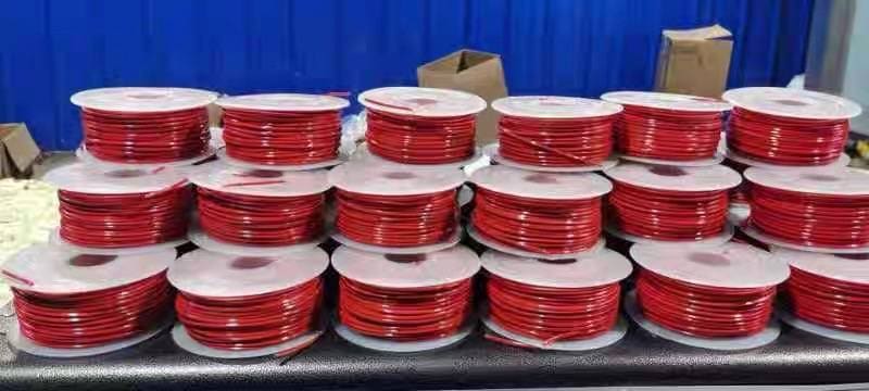 Three rows of stacked red TS thermosensitive cable spools on a black workbench against a deep blue panel — Aetherm TS series production samples