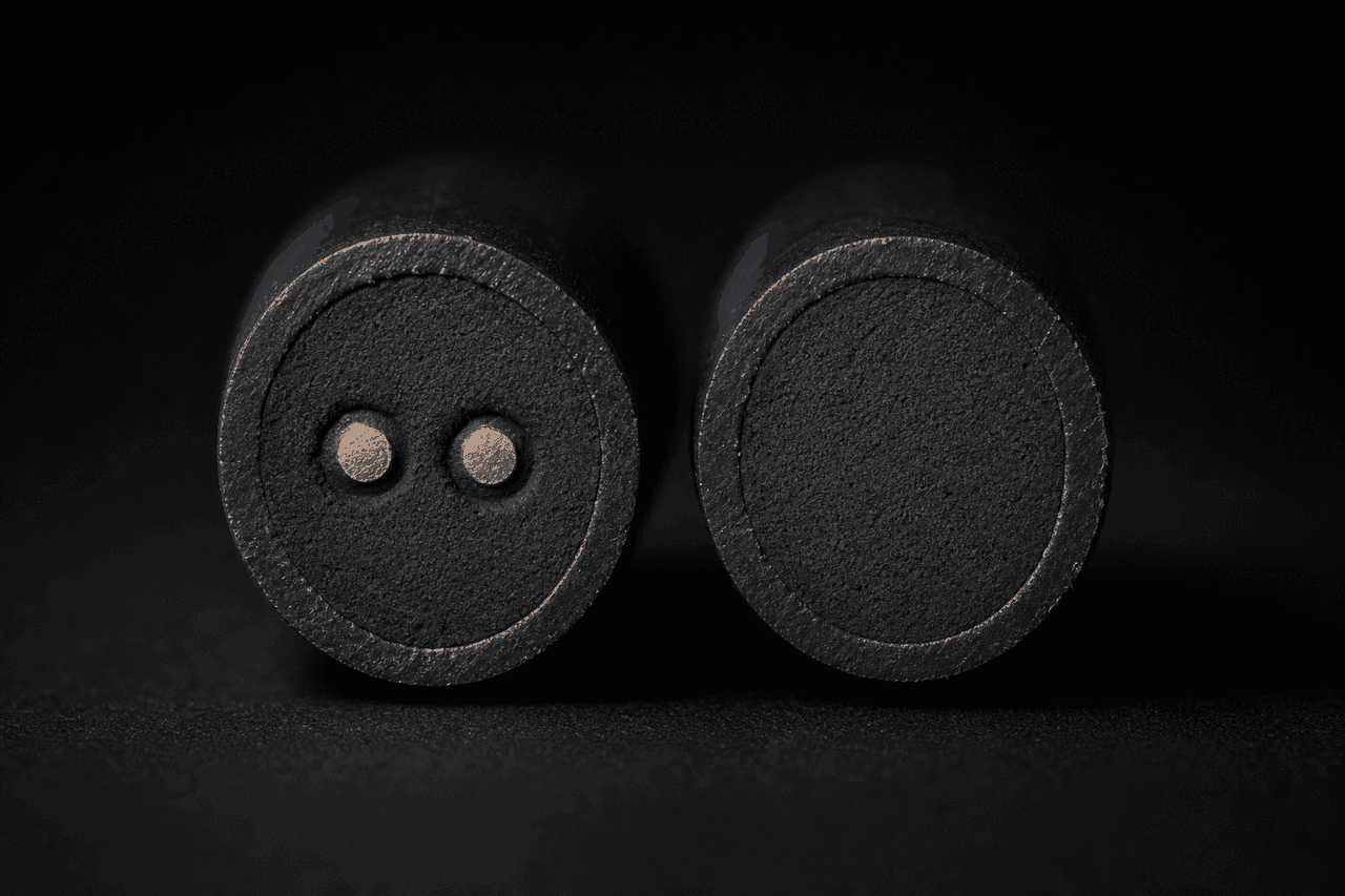 Two thermal sensor cable cut ends mounted vertically side by side on a matte black surface — the left cable cross-section reveals a metal-core architecture with two metallic conductor dots embedded in the dark thermosensitive compound, the right cable cross-section reveals a non-metal-core architecture with a uniform compound block and no continuous metallic conductor pair; studio macro lighting against a deep black background isolates the two architectures so the only visual difference is the cross-section itself — the row that decides which architecture the panel actually reads.