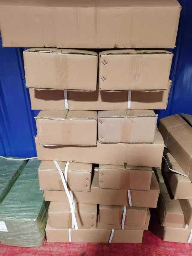 Stack of cardboard shipping cartons strapped with packing tape, with a blue softpack bundle on the side and a red anti-slip mat on the floor